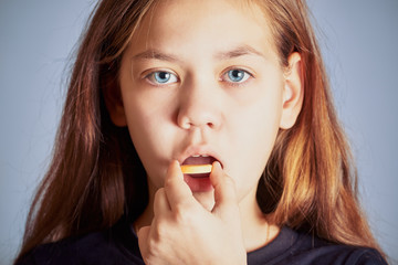 Sick girl with blue eyes puts big yellow pill in her mouth.