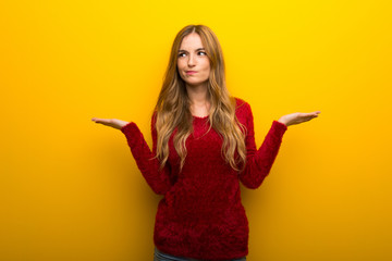 Young girl on vibrant yellow background having doubts while raising hands and shoulders