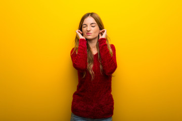Young girl on vibrant yellow background covering ears with hands. Frustrated expression