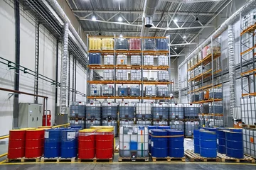 Wall murals Industrial building Oil drums and plastic container on pallets in a warehouse on metal shelving. Handling and storing industrial lubricants. Hazardous material storage. Red and blue tank