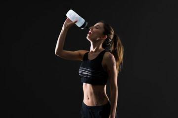 Sport woman with a bottle of water on dark background