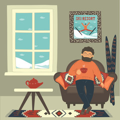 Man in cozy armchair drinking hot tea in the room near window on ski resort. 