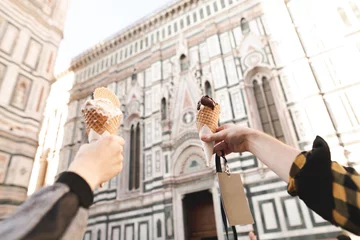 Fotobehang Hands hold the traditional Italian gelato ice cream. Couple holding ice cream gelato on background Cattedrale di Santa Maria del Fiore, Florence, Italy © bodnarphoto