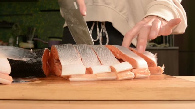 Close-up of female hands are cutting with a knife a large salmon on a wooden table of home cooking