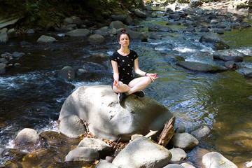 Beautiful girl meditates sitting on a stone.