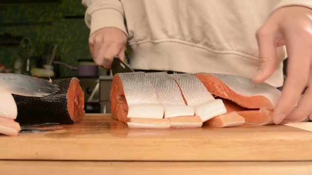 Close-up of female hands are cutting with a knife a large salmon on a wooden table of home cooking