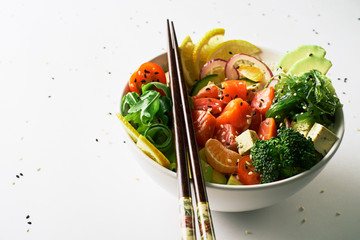 poke bowl with salmon, avocado, cucumber, arugula, broccoli, rice, carrot and sweet onions with chuka salad, chopsticks isolated over white background. side view close-up