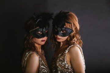 Portrait of two women dancers in max-size masks and gold dresses
