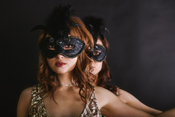 Portrait of two women dancers in max-size masks and gold dresses