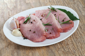 Raw pork meat sliced with pepper. rosemary. garlic and bay leaves in white plate on old wooden table