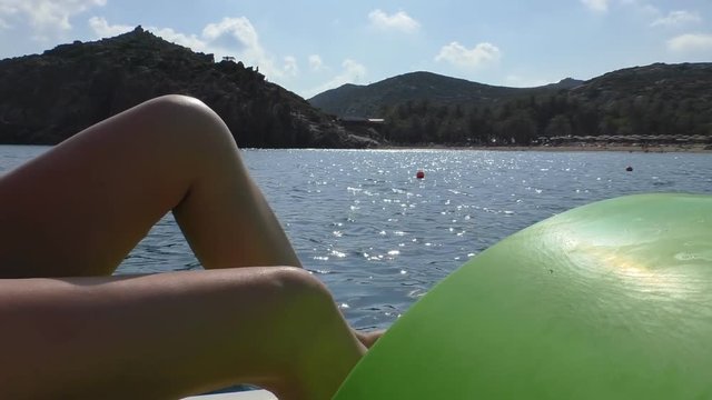 Close up of legs of woman pedaling pedalling pedal boat in the Mediterranean sea with beach and mountains on Crete island seaside in the background