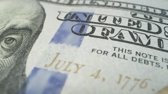Panning across 100 dollar bill in maco view from angle distorting aspect of Benjamin Franklin.