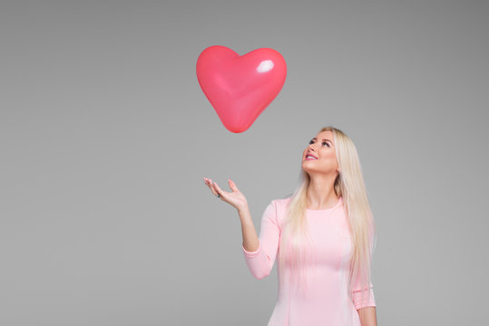Beautiful young blond woman with pink heart shape air balloon on grey background. Woman on Valentine's Day. Symbol of love - Image. Space for text