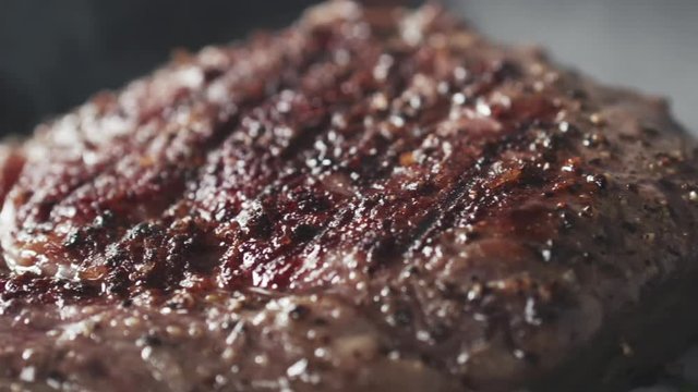Slide slow motion shot of cooking rib eye steak with herbs on grill pan