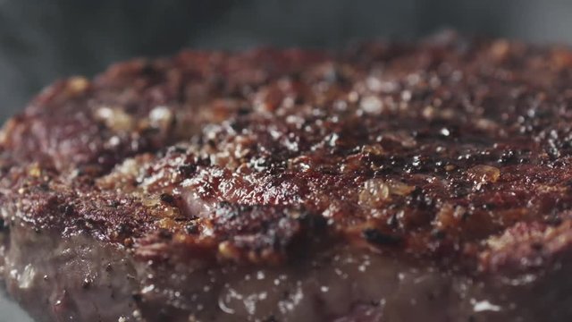 Slide slow motion shot of cooking rib eye steak on grill pan
