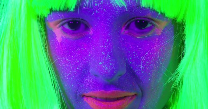 Closeup woman face with fluorescent make up in green, wig, creative makeup look great for nightclubs. Halloween party, shows and music concept - slow motion video