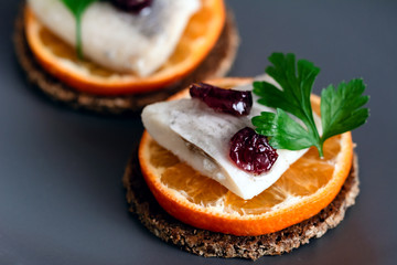Salted herring on rye bread and tangerine, decorated with cranberry and parsley. Appetizer food