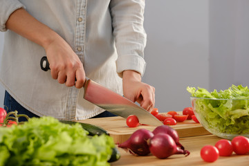 Girl cuts fresh tomatoes for a delicious salad. A variety of fresh vegetables on a wooden table.