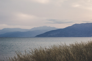 romantic melancholy soft focus landscape with dry grass on foreground and sea bay calm water surface and mountain range on background in morning sunrise foggy cloudy weather time 