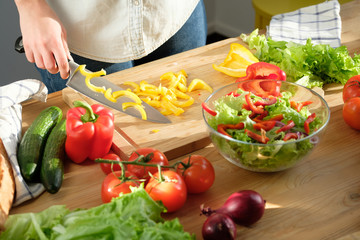 Girl cuts sweet pepper in vegetable salad. Cooking salad.
