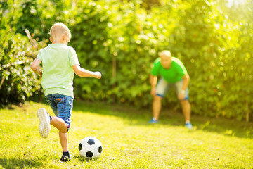 Son playing with his father footbal in a park, having fun