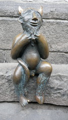 Obraz premium Small smiling devil figure made of bronze sits on a stone wall 