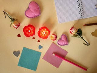 Decorative composition for congratulations with Valentines, wedding, birthday from fresh roses, rose petals, felt hearts, lit candles, empty notebook for records, paper, pencils on a light background,