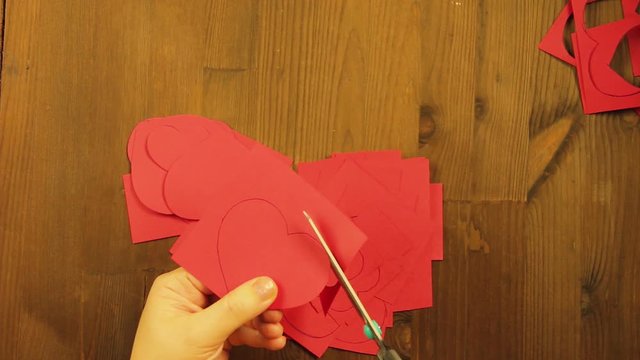 The girl cuts hearts from red cardboard. Close-up