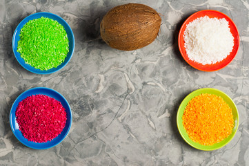Coconut near colored coconuts flakes in colored plates on old gray concrete with copy space. Flat lay