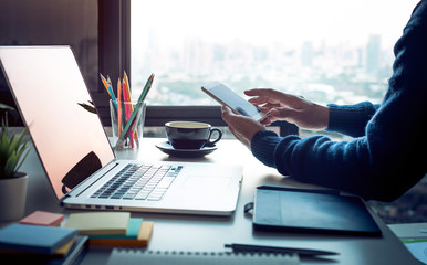 Fototapeta premium Young man using smartphone with modern work table and computer laptop and cityscapes view from window.Business concepts ideas.Strategy analysis