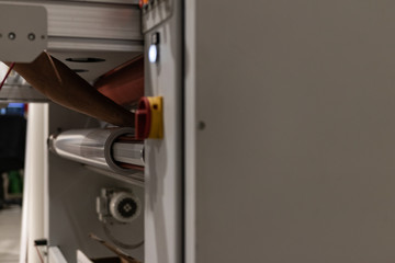 Operating a big printing machine and laminator, armed with red rolls and vinyl transparent film....