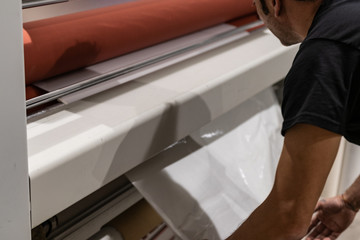 Operating a big printing machine and laminator, armed with red rolls and vinyl transparent film....