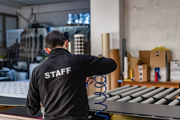 Specialized staff working big vinyl rolls on a professional printing machine. Details of the laminator and paper feed. 