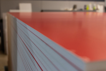 Professional material printing facility, big vinyl sheets, ready for large sound proofing projects. Glossy, matte, ecological architectural elements stacked and piled. White foam, red layers.