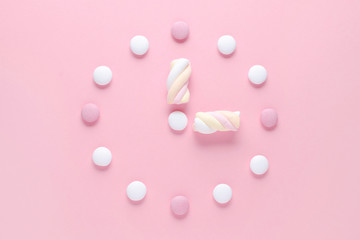 concept image, a clock with candy and marshmallow, pastel colors on pink