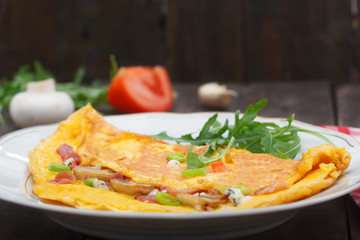 Omelette stuffed with ham, cheese and mushrooms on a plate. Omlet breakfast on old wooden table.