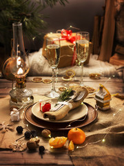 Christmas table. It is a plate with a napkin. Near ancient candle, festoon, glasses of champagne, tangerines and nuts.