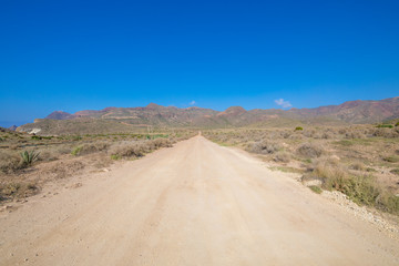 straight dirt road in Cabo de Gata Natural Park with mountains in horizon (Cabo de Gata in Spanish), wild and famous touristic destination in Almeria (Nijar, Andalusia, Spain, Europe)