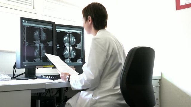 Young woman doctor examines the results of patient female breast cancer research on the computer. Mammogram showing localization of breast cancer. The surgeon can locate the exact area for excisional 