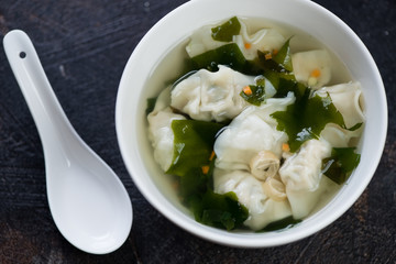 White bowl of wonton soup on a dark brown stone background, close-up, view from above