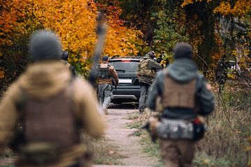 Men with guns go for a black jeep against the backdrop of the autumn forest