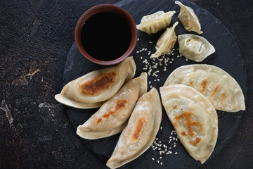 Various types of fried korean dumplings with a dipping sauce, flatlay on a dark brown stone background, closeup