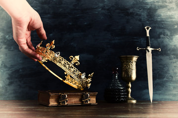 low key photo of king holding gold crown and sword. fantasy medieval period.