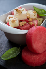 Close-up of salad with fresh watermelon, melon and nuts served in a white bowl, selective focus, vertical shot