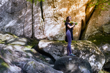 Young attractive girl in the mountains is holding a yoga mat