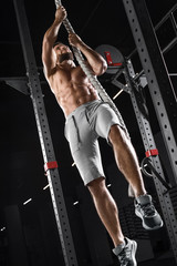 Crossfit athlete climbing up the rope in the gym. Muscular man doing exercise, naked torso abs
