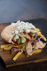 Greek chicken gyros with tzatziki sauce on a rustic wooden serving board, vertical shot with space