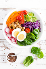 Buddha bowl salad with chickpeas, sweet pepper, tomato, cucumber, red cabbage kale, fresh radish, spinach leaves and boiled egg, healthy eating concept, top view, flat lay