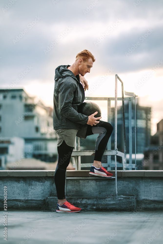 Wall mural Athlete standing on rooftop staircase looking  down - Wall murals