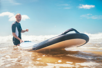 Naklejka premium Selective focus with wide open aperture of long surf board on ocean waves with unfocused Young Man surfer on the background. Learning surfing concept.